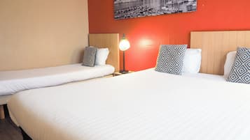 A hotel room with two single beds, a nightstand with a lamp, and a wall-mounted picture.