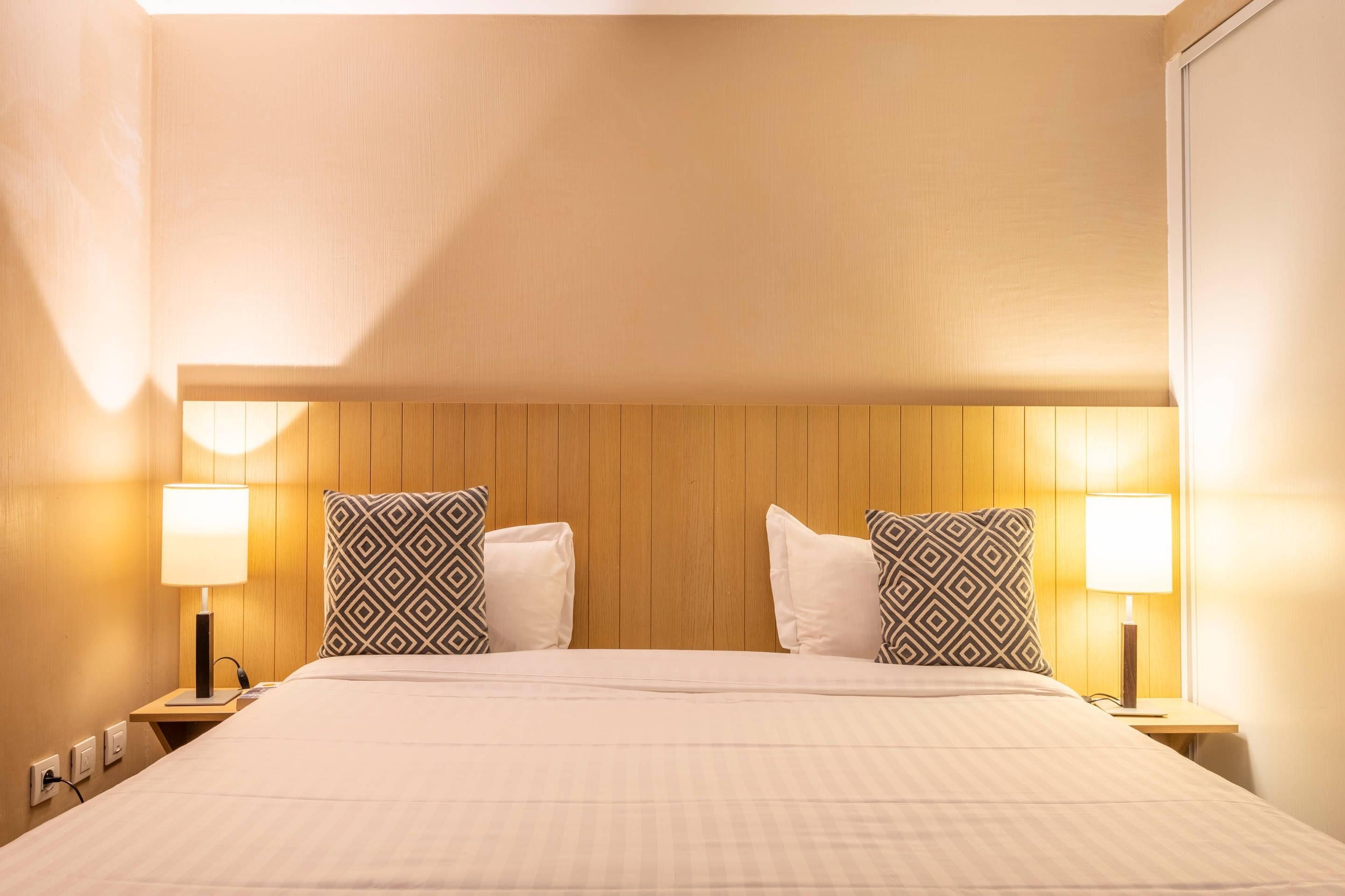 Habitació d'hotel amb un capçal de llit de fusta, dues làmpades de nit, un llit amb estovatge blanc i almoines estampades.