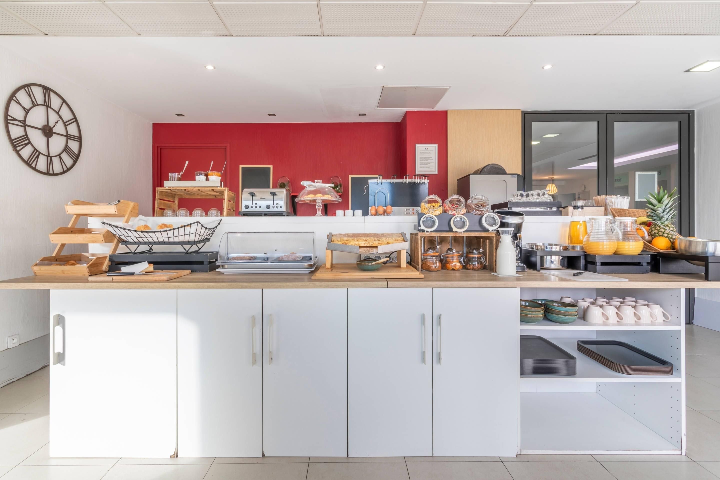 Une cuisine moderne avec un mur d’accent rouge, une horloge et divers appareils et ustensiles de cuisine.