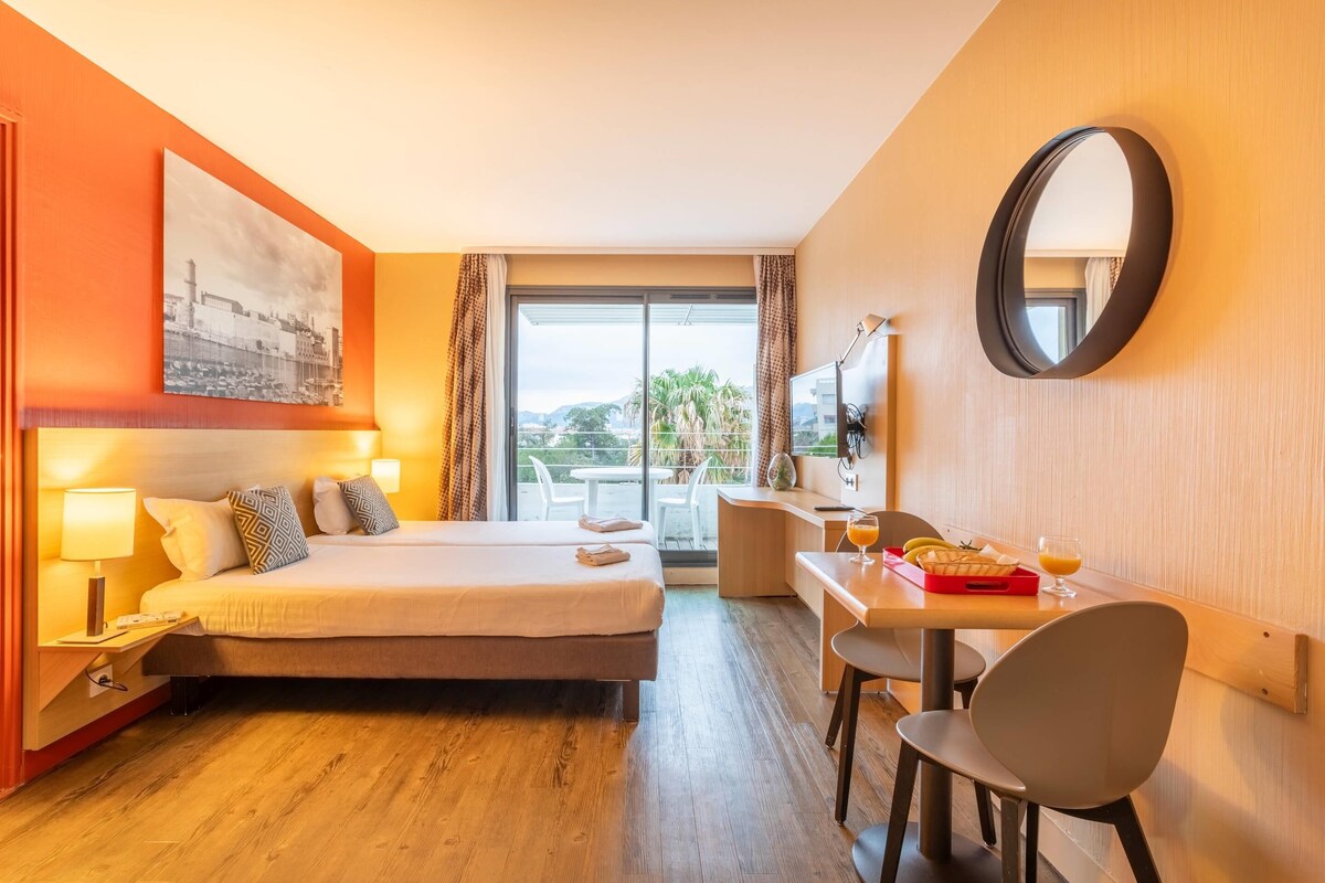 Een hotelkamer met een bed, bureau, stoel en een groot raam.