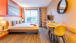 A hotel room with a bed, desk, chair, TV, and a large window with a view.