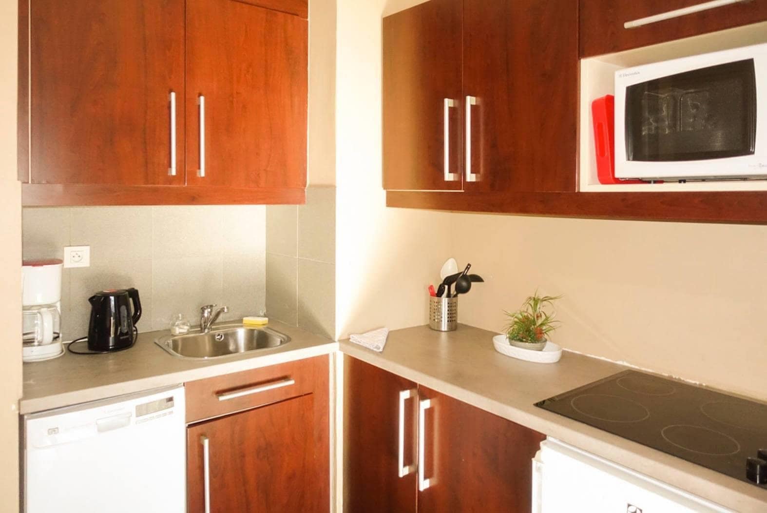 A kitchen with wooden cabinets, a microwave, a stove, a sink, and a coffee maker.