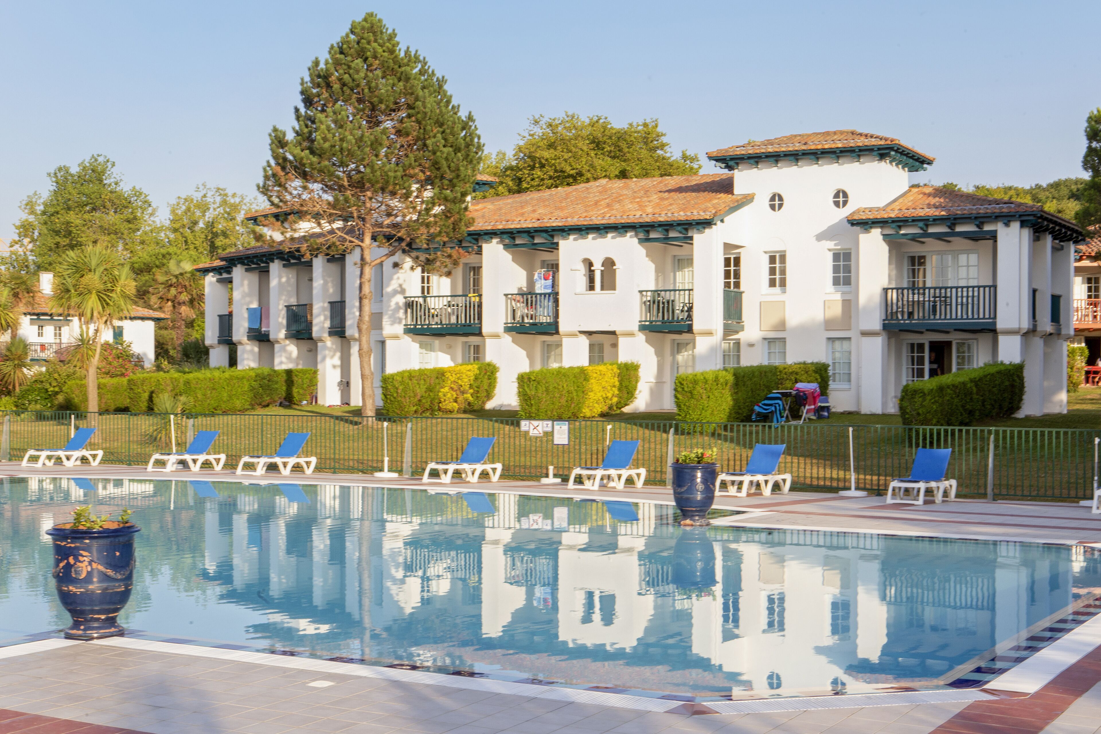 A pool with lounge chairs and a building with balconies in the background.