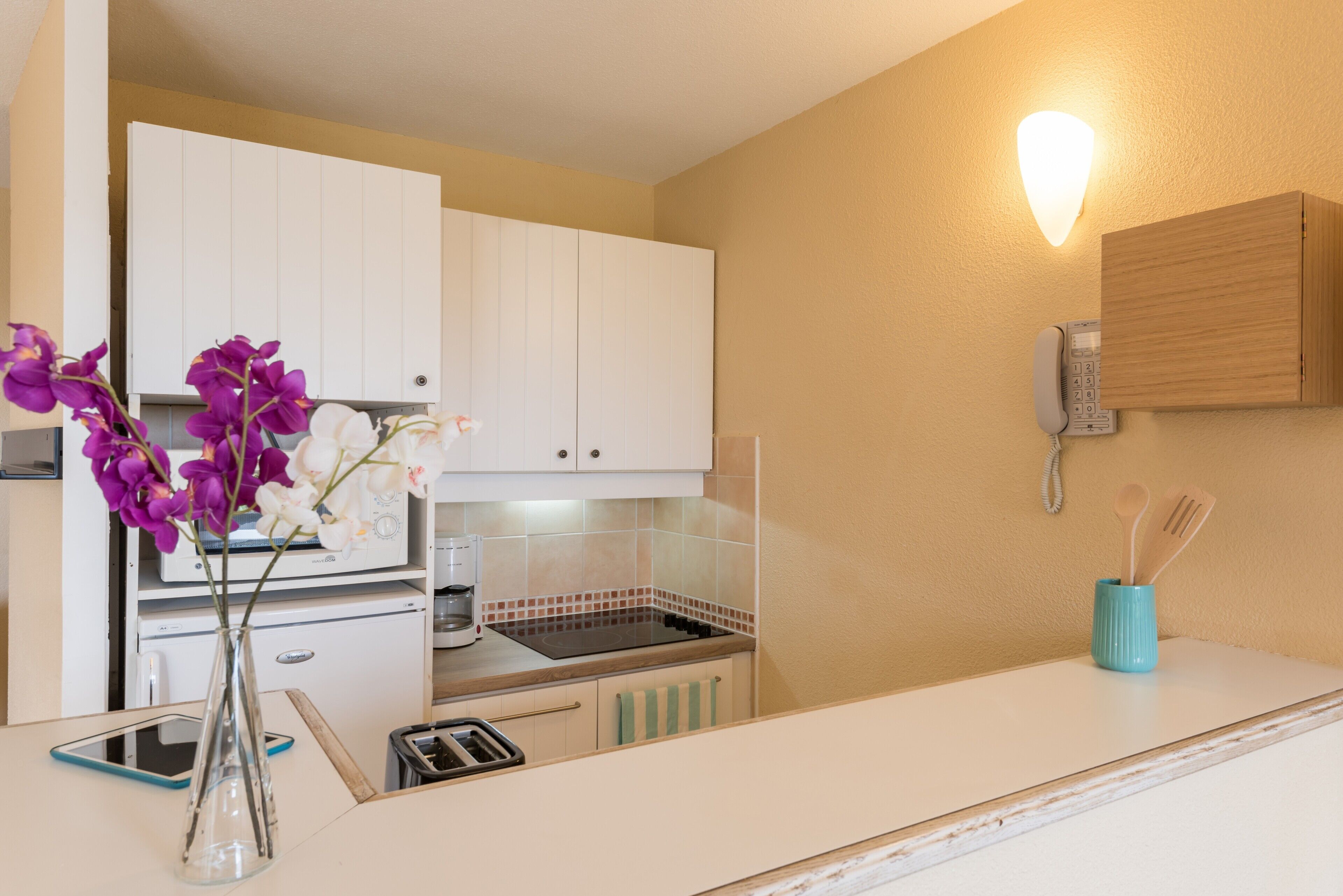 A kitchen with white cabinets, a stove, a coffee maker, a phone, and a vase with flowers.