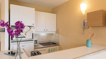 A kitchen with white cabinets, a stove, a coffee maker, a phone, and a vase with flowers.