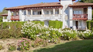 A large, two-story building with a red-tiled roof, multiple balconies, and a well-maintained garden with various flowering plants. - Pierre & Vacances Residence Le Domaine de Bordaberry (Urrugne)