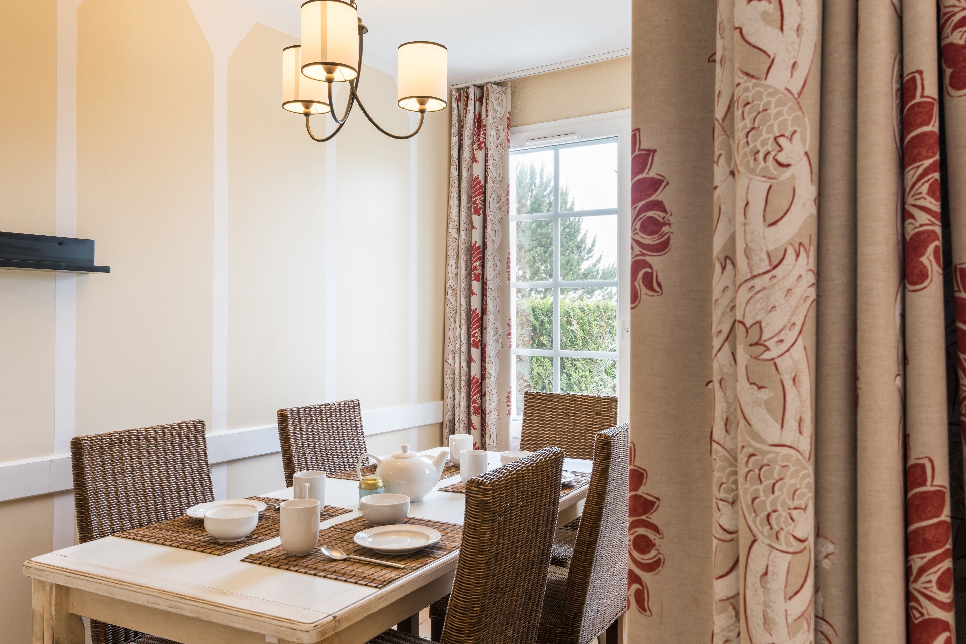 Un comedor con una mesa dispuesta para cuatro, incluyendo platos, tazones y vasos. Hay sillas de mimbre y un candelabro sobre la mesa.