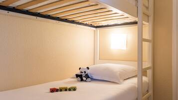 Un lit superposé avec un matelas blanc, une petite fenêtre laissant entrer la lumière du jour, et un ours en peluche et des voitures jouets sur le lit.