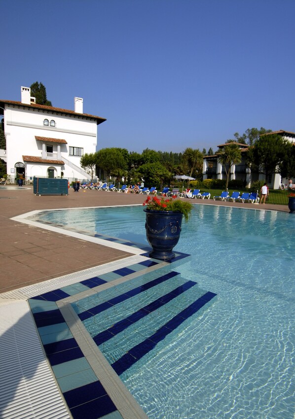 Un área de piscina con un deck de baldosas, sillas de descanso y una maceta grande con flores.
