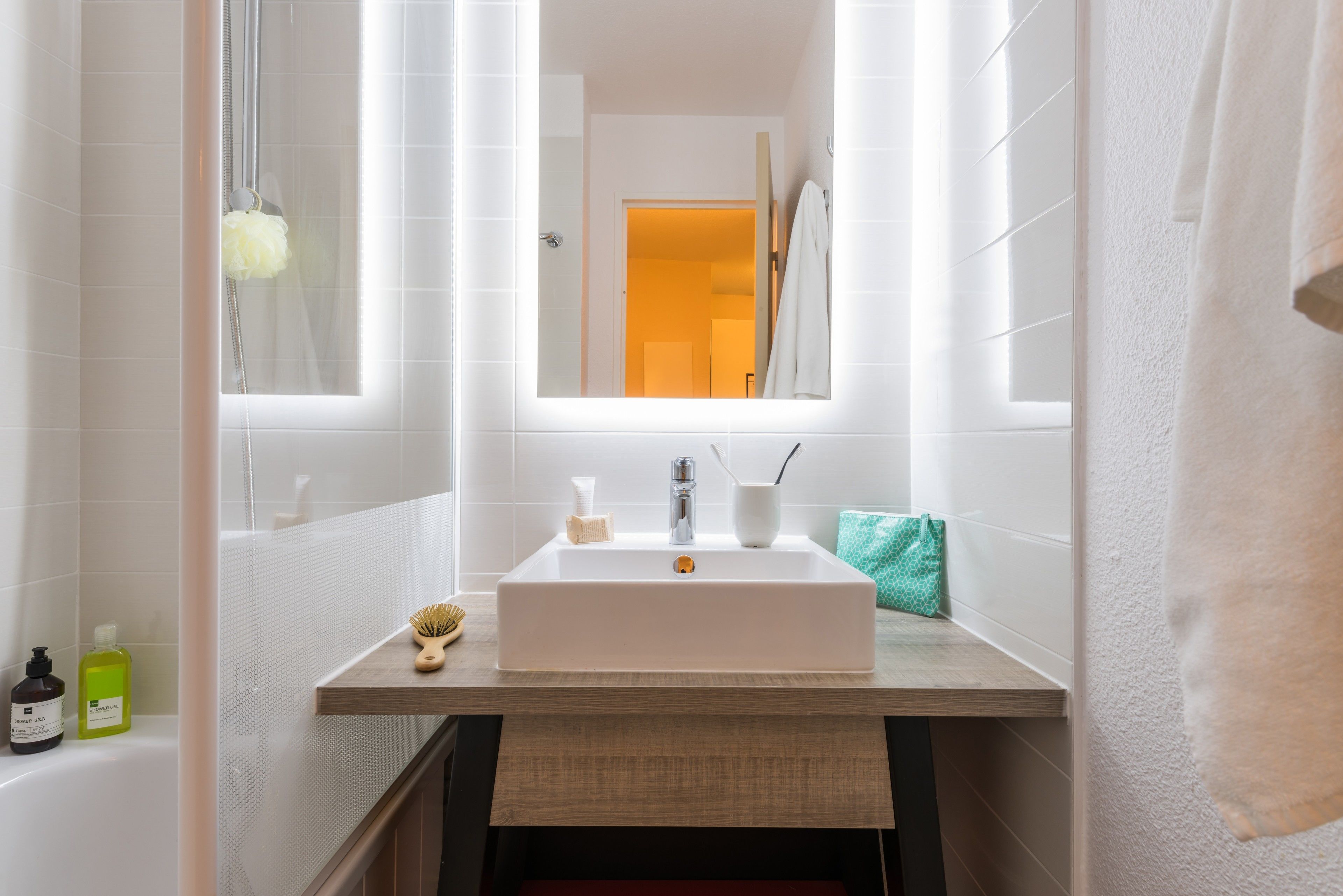 Un baño moderno con un lavamanos blanco, espejo y vista al pasillo.