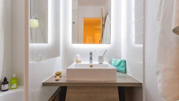 Un baño moderno con un lavamanos blanco, espejo y vista al pasillo.