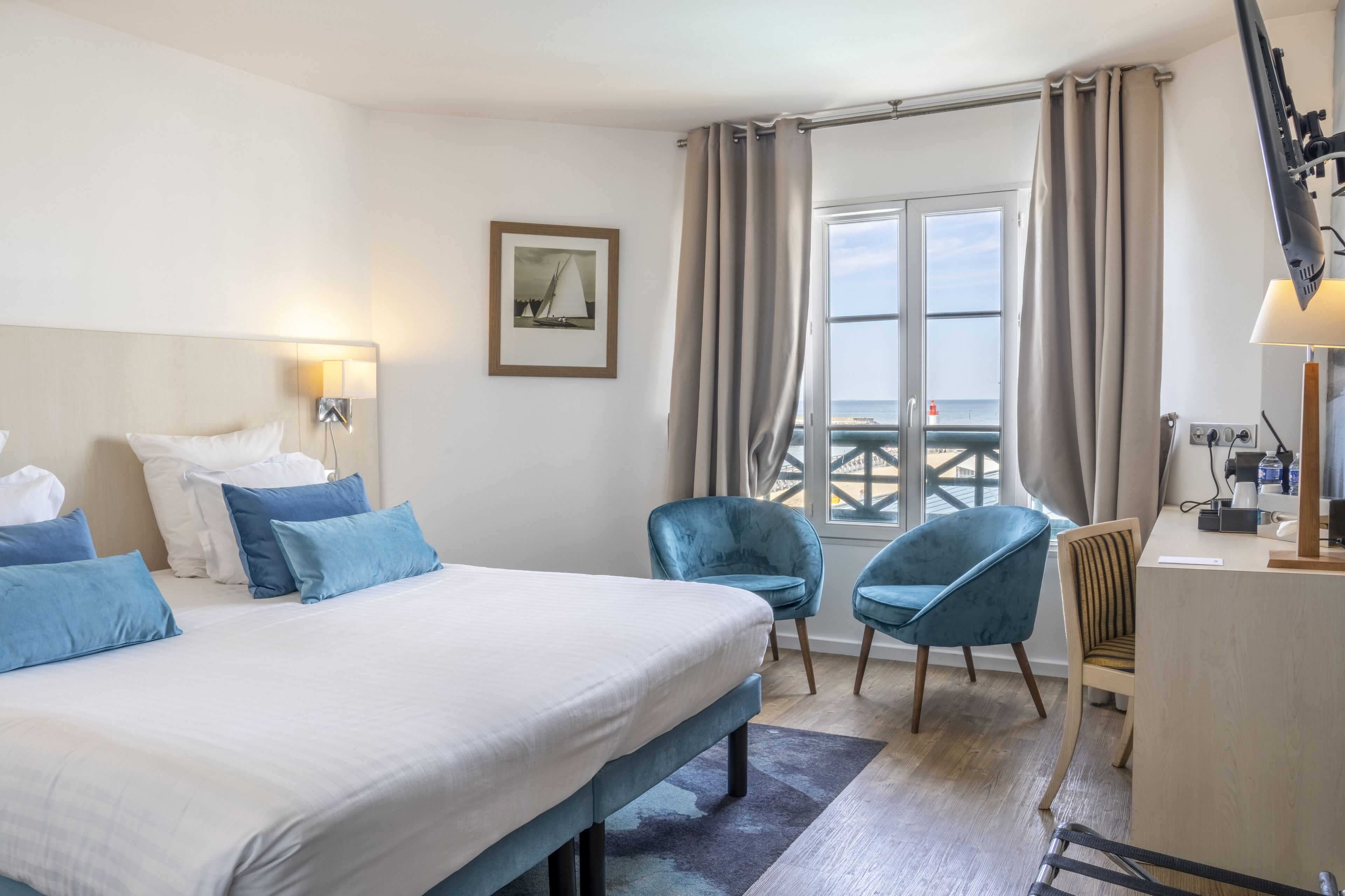 A hotel room with a large bed, two chairs, a desk, and a window with curtains.