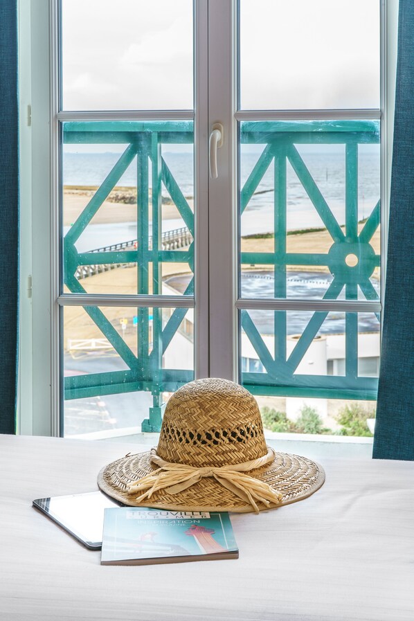 Habitación con vista a la costa a través de una ventana con estructura metálica geométrica.