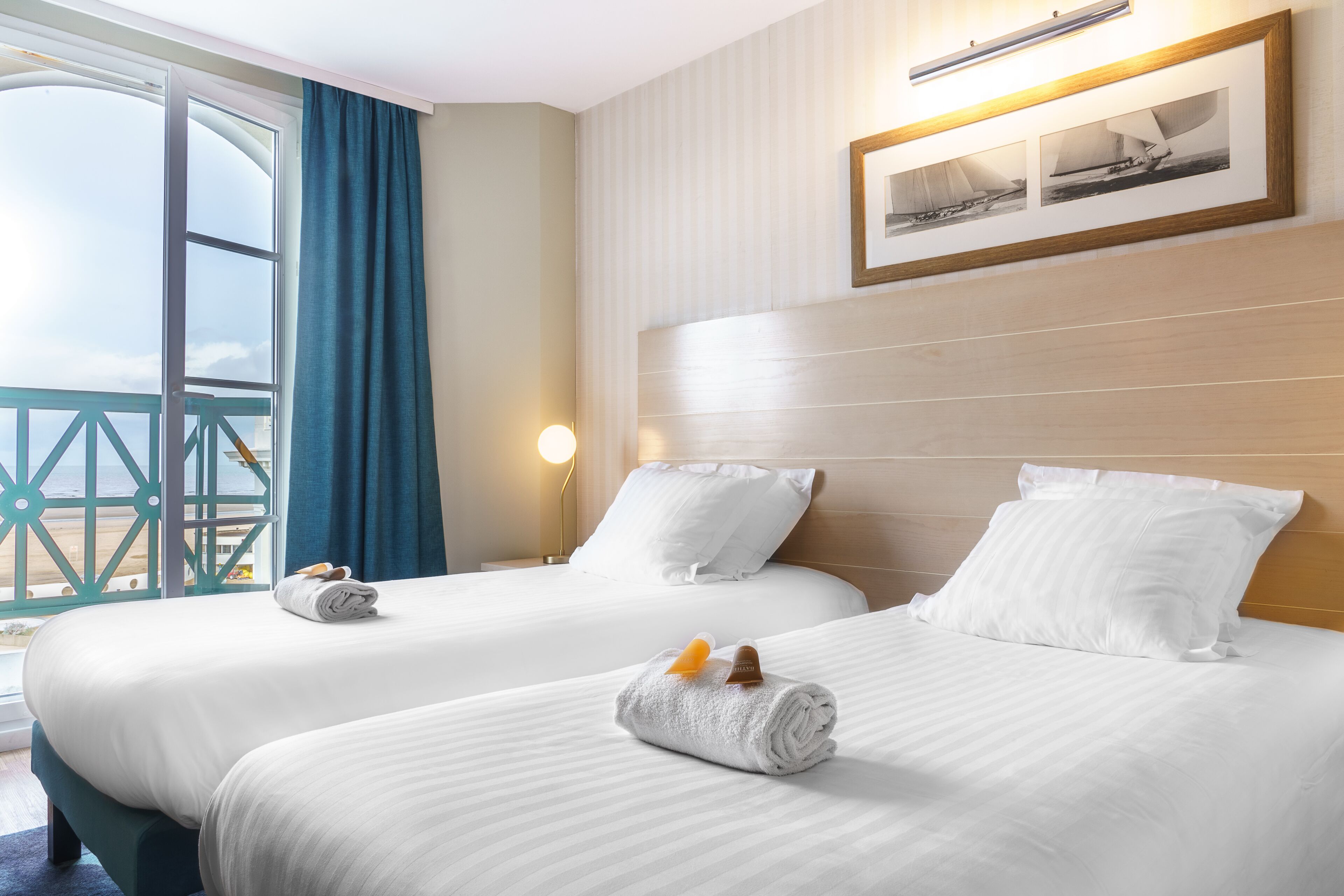 A hotel room with two beds, a large window with a view of the sea, and a framed picture on the wall.