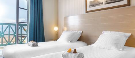 A hotel room with two beds, a large window with a view of the sea, and a framed picture on the wall.