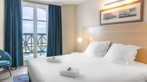 Et hotelværelse med seng, natbord, lampe, stol og en balkon med gardiner.