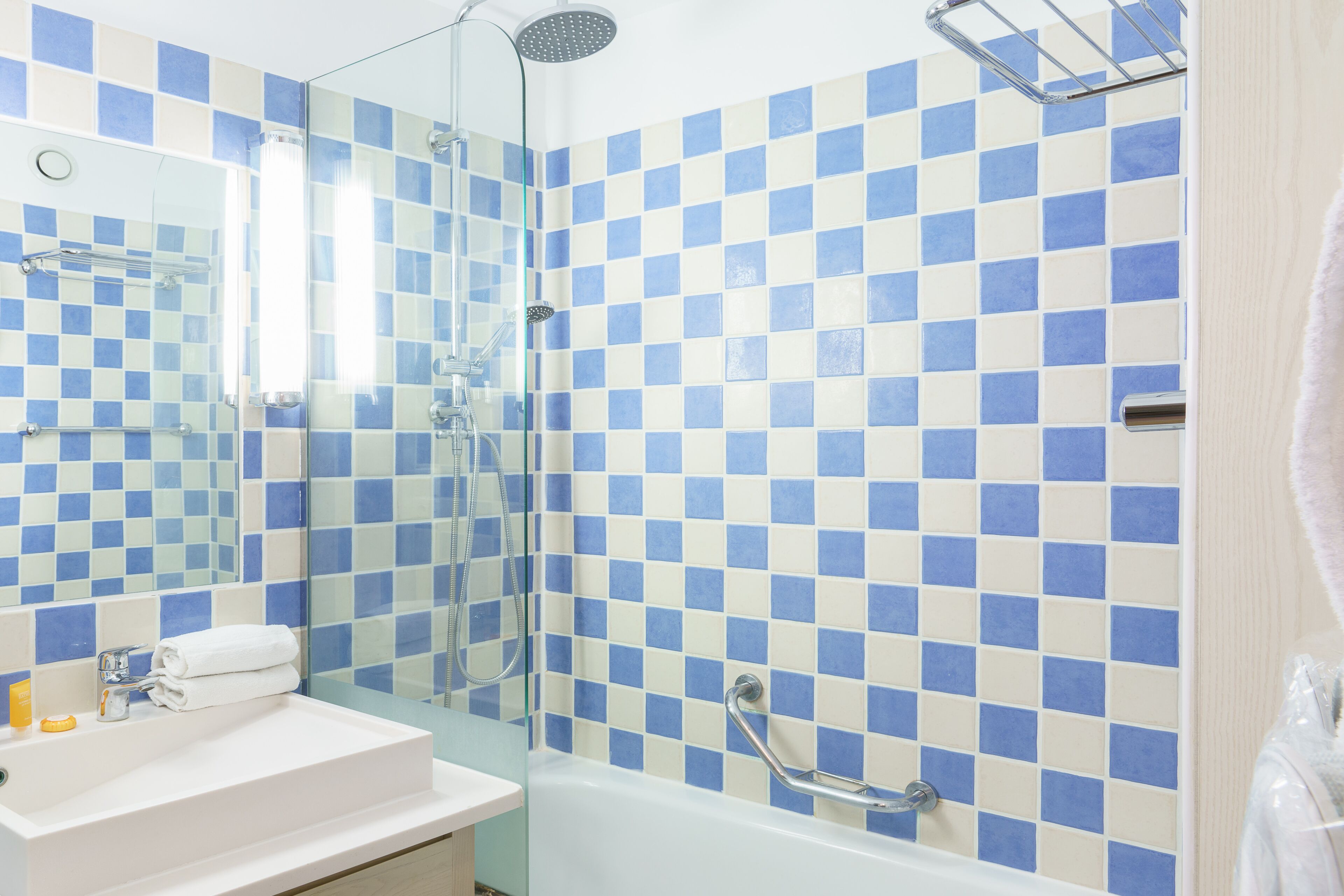 A bathroom with a checkered blue and white tile wall, a glass shower enclosure, a white sink with a towel, and a handheld showerhead.