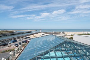 Vista desde un punto elevado sobre una zona costera con un edificio de techo de cristal, un muelle y una playa.