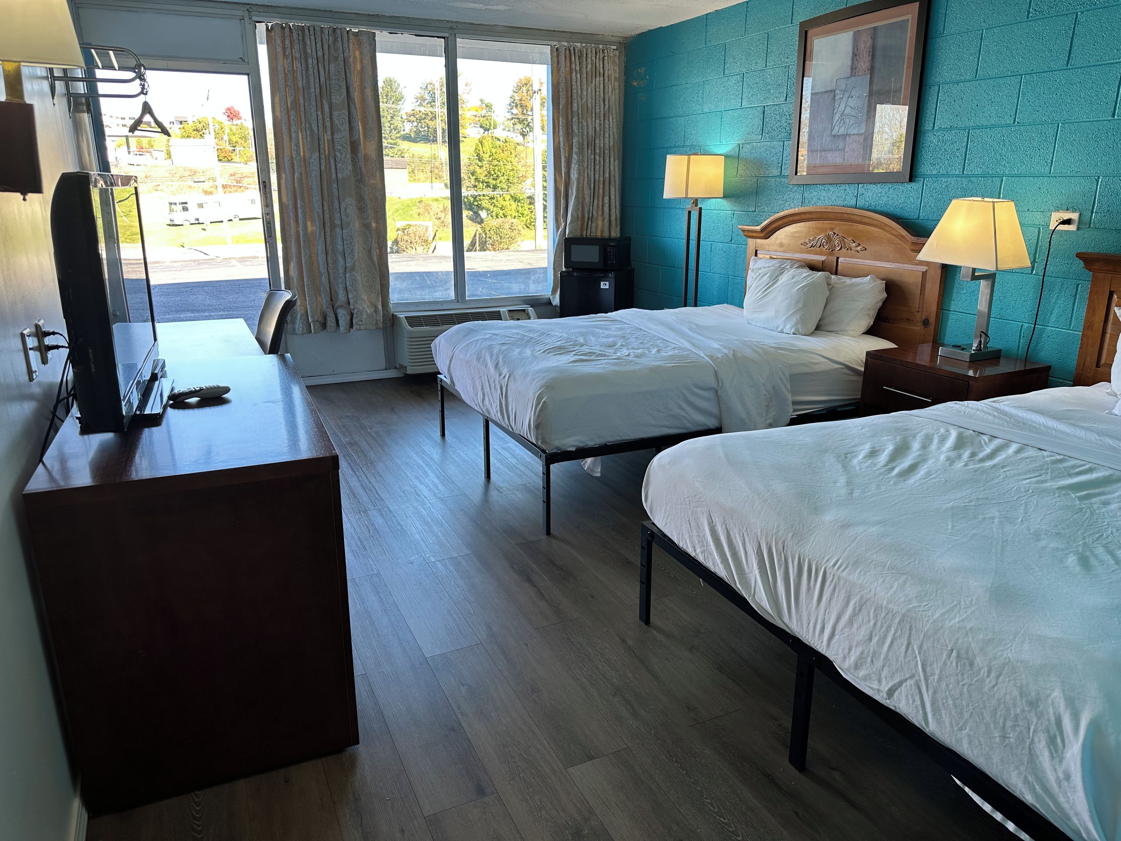 A hotel room with two beds, a desk, a television, and a window with curtains.