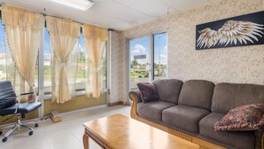 A living room with a sofa, a wooden coffee table, a black office chair, and a large window with curtains. - Americas Best Value Inn Wytheville (Wytheville)