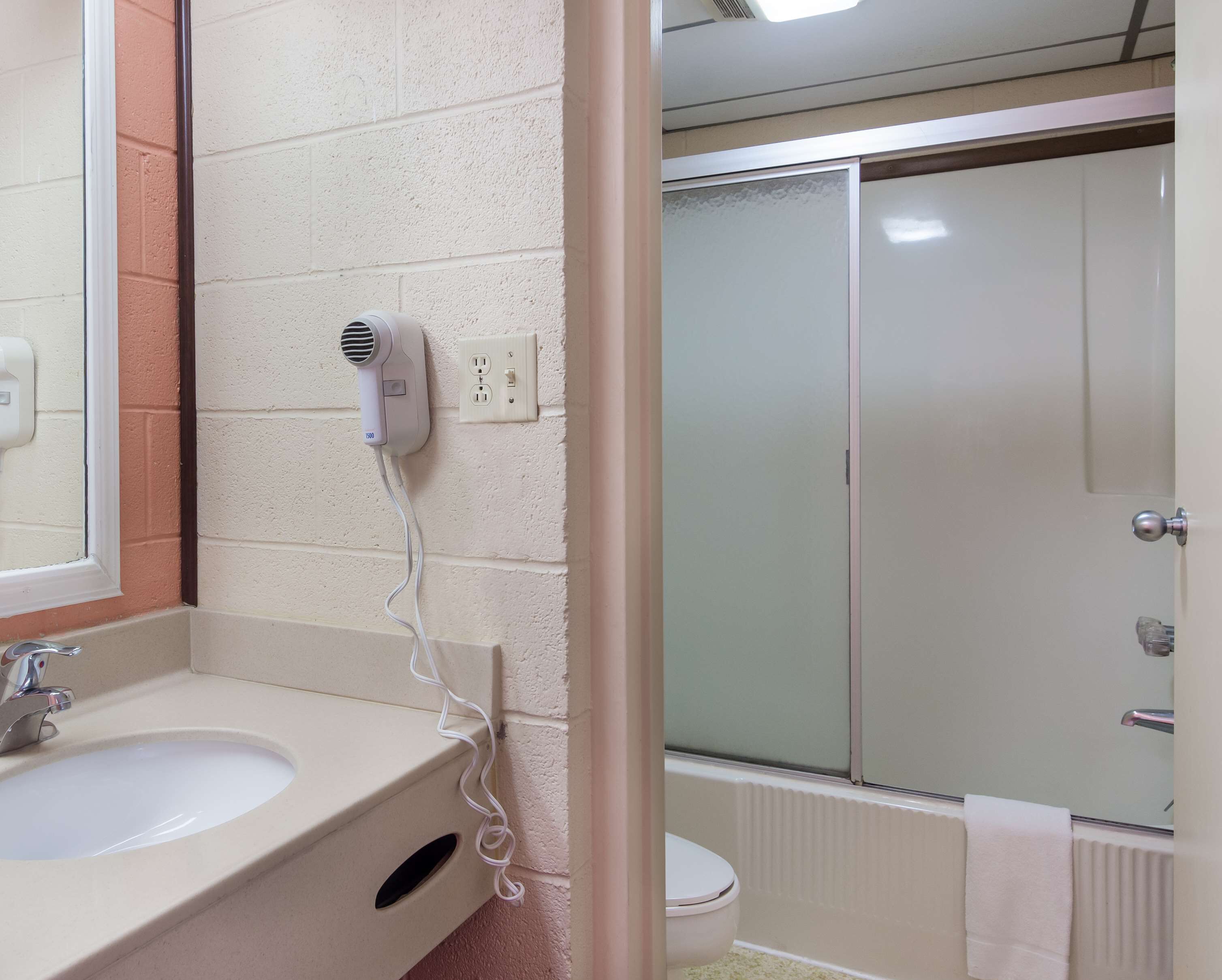 A bathroom with a sink, a hairdryer, a toilet, and a shower area.