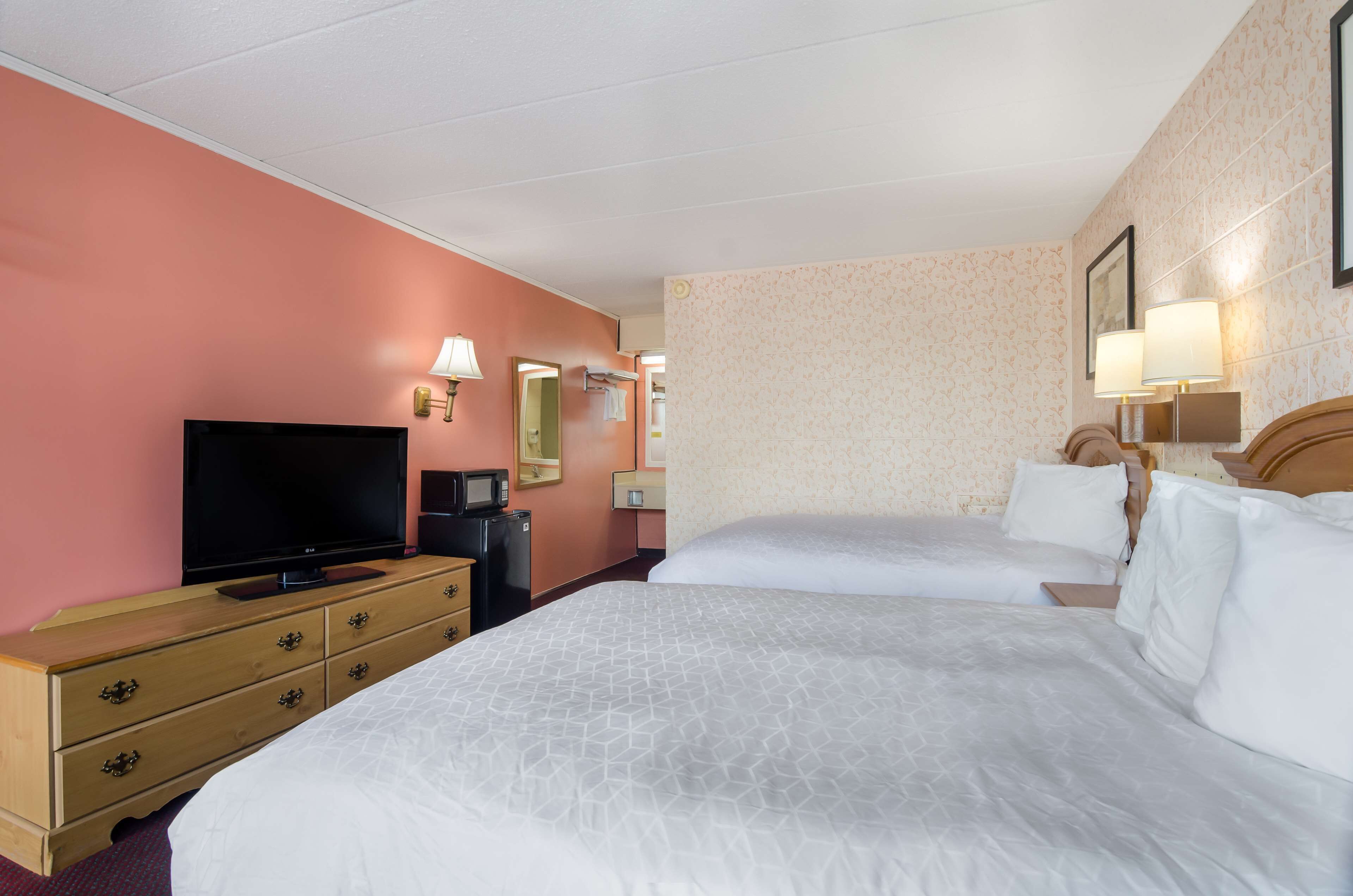 A hotel room with two beds, a television, a dresser, and a microwave.
