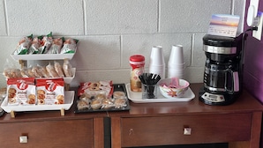 A breakfast setup with pastries, coffee, and a coffee maker on a counter. - Americas Best Value Inn Wytheville (Wytheville)