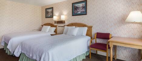 A hotel room with two beds, a wooden table, a chair, and two wall-mounted lamps.