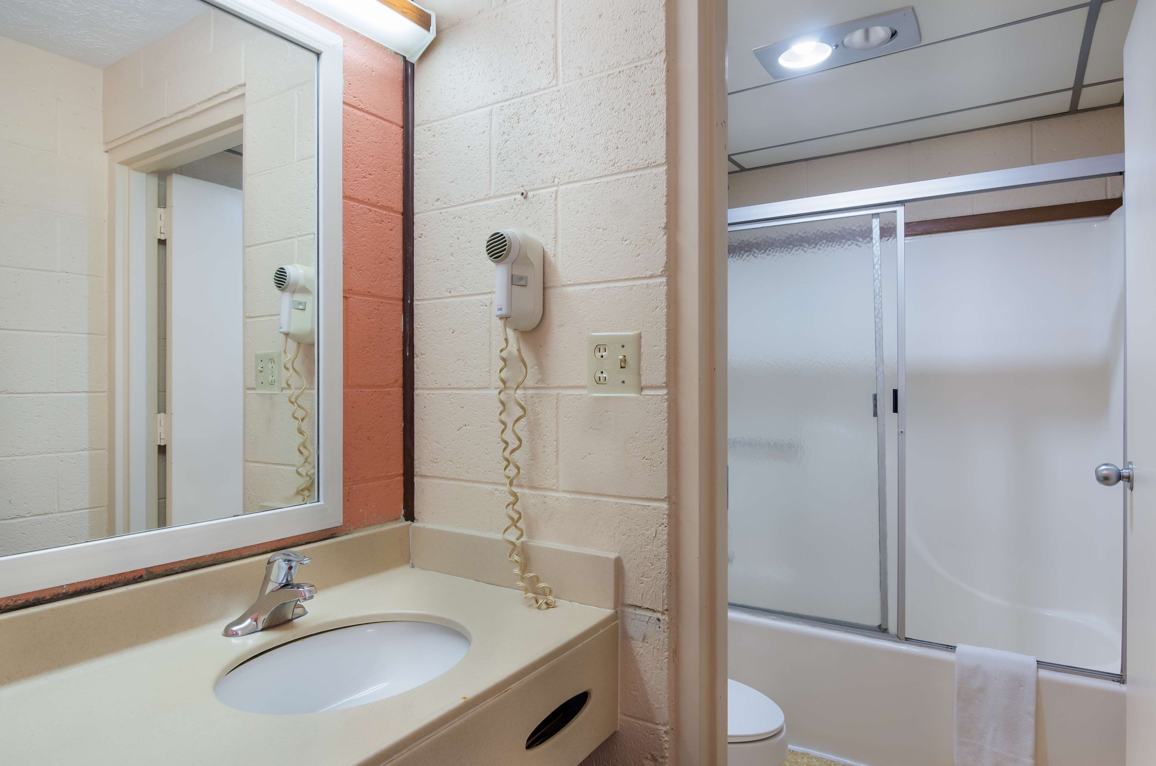 A bathroom with a sink, mirror, hairdryer, and a shower area.