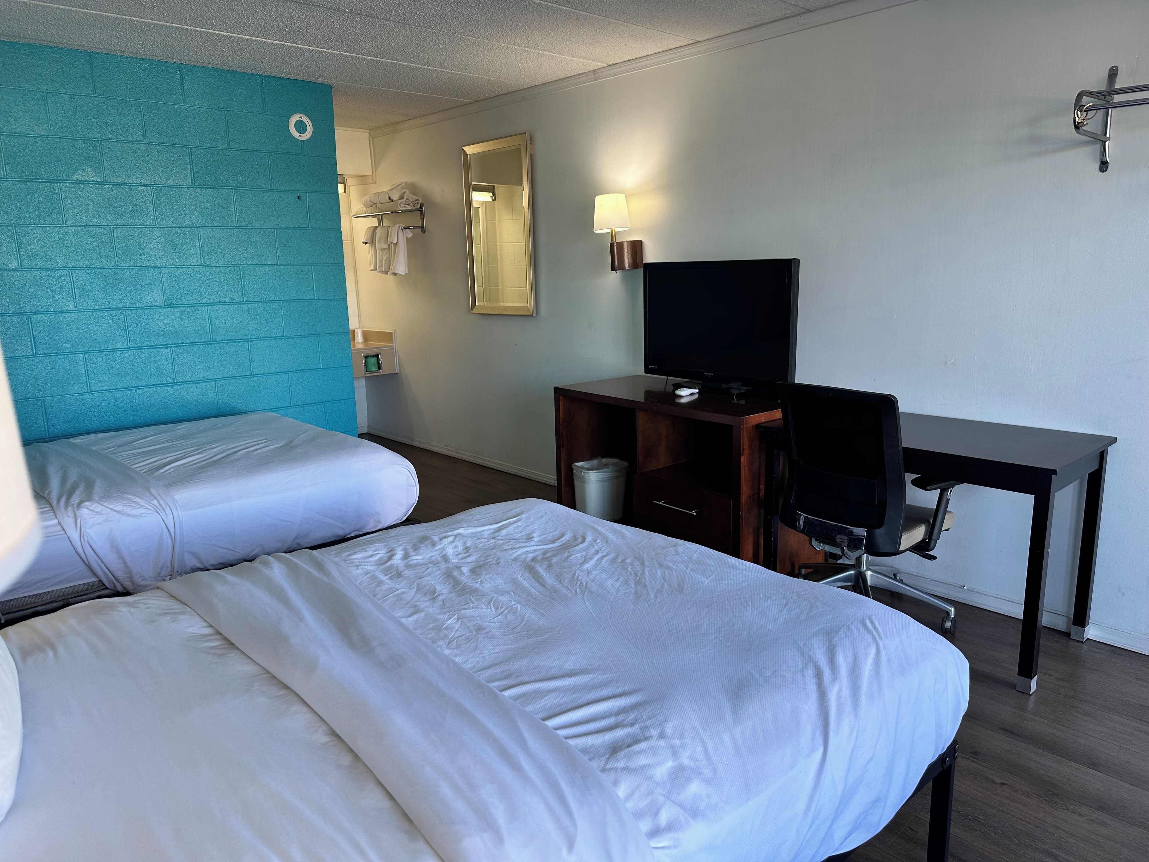 Een hotelkamer met twee bedden, een bureau met een televisie, een spiegel en een wandlamp.