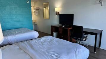 Een hotelkamer met twee bedden, een bureau met een televisie, een spiegel en een wandlamp.