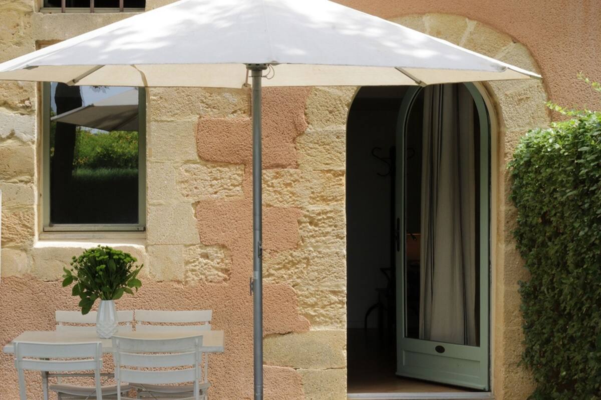 A stone building with a white umbrella table and chairs, a potted plant, and a door leading to an interior space.