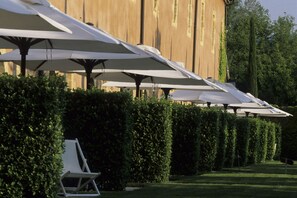 A row of white umbrellas and lounge chairs in a well-manicured garden with a wooden building in the background. - La Bastide du Roy Rene (Aix-en-Provence)