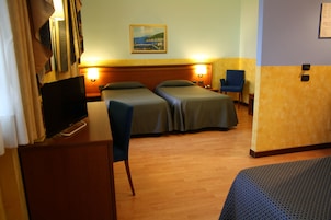 Habitación de hotel con dos camas, un escritorio con televisor y un cuadro en la pared.