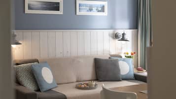 A cozy living room with a wooden panel wall, a beige sofa with patterned cushions, a small table with a tray of snacks, and two framed pictures on the wall.