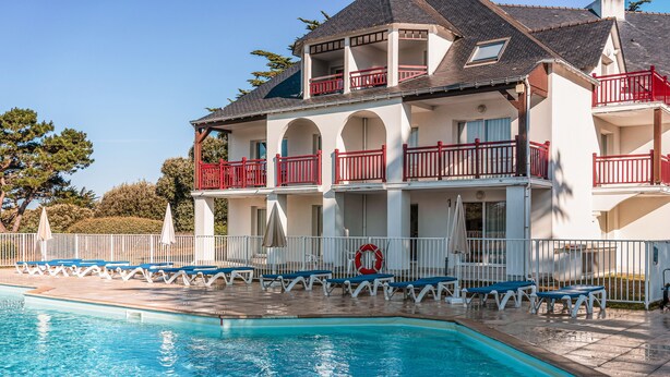A multi-story hotel with a swimming pool, red balconies, and white railings. - Pierre & Vacances Premium Le Domaine de Cramphore (Le Pouliguen)