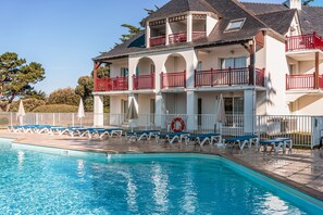 Ein mehrstöckiges Hotel mit Schwimmbad, roten Balkonen und weißen Geländern.