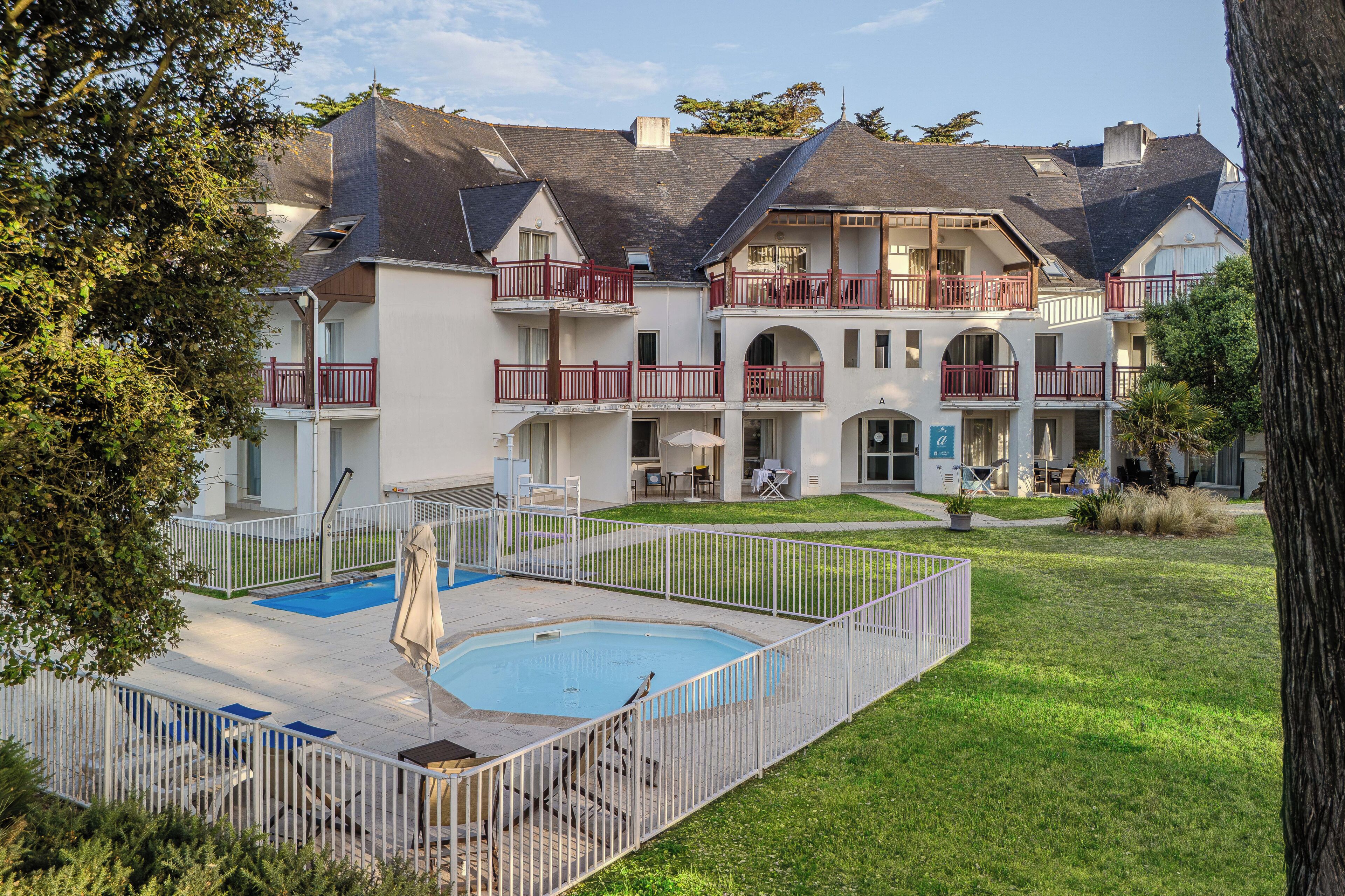 A multi-story building with balconies, a swimming pool, and a well-maintained lawn.