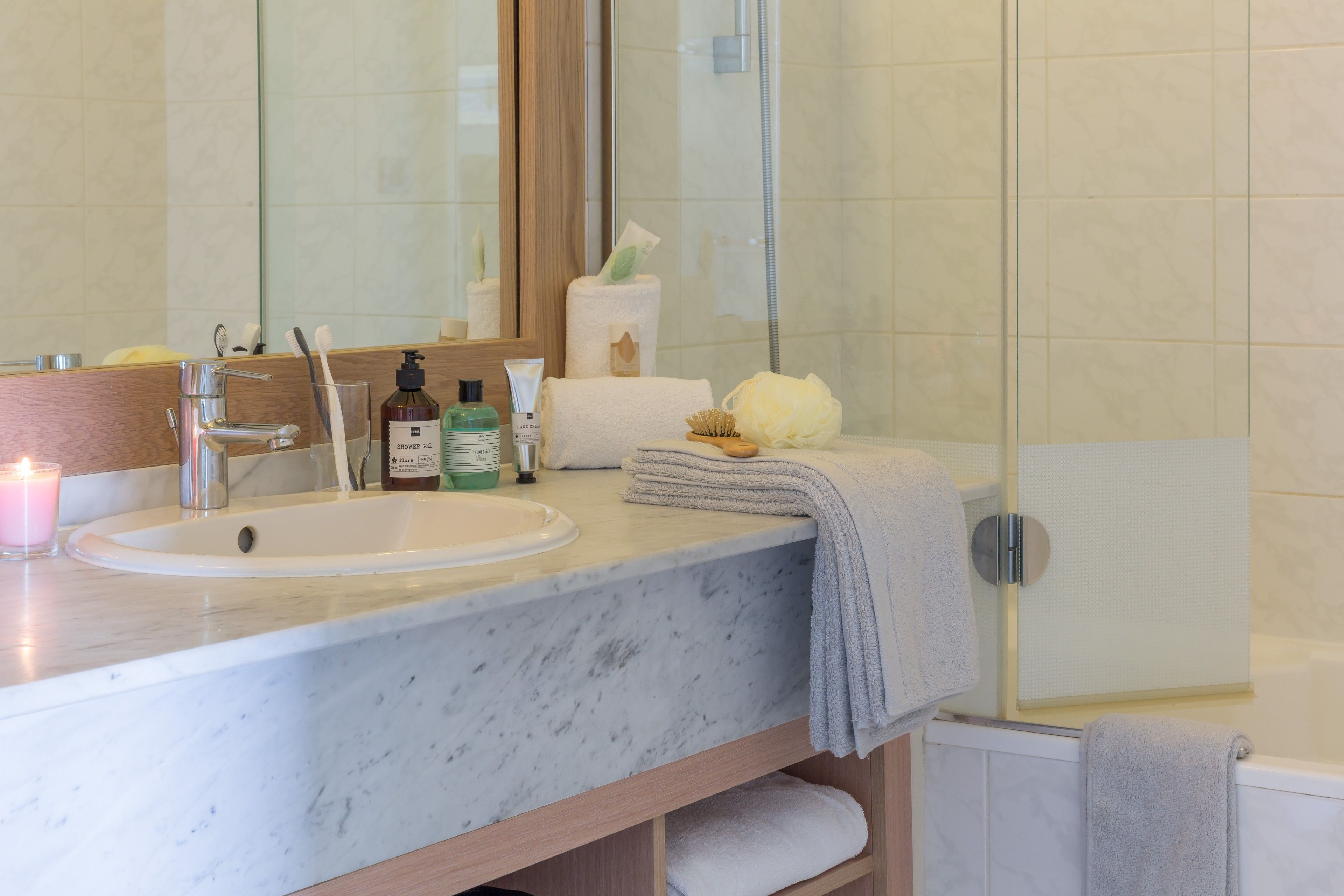 Une salle de bain avec un lavabo en marbre, un miroir, une cabine de douche en verre et un porte-serviettes.