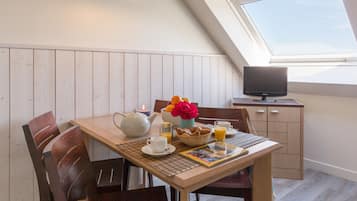 Un área de comedor con una mesa dispuesta para el desayuno, un televisor sobre un mueble bajo y un tragaluz arriba.