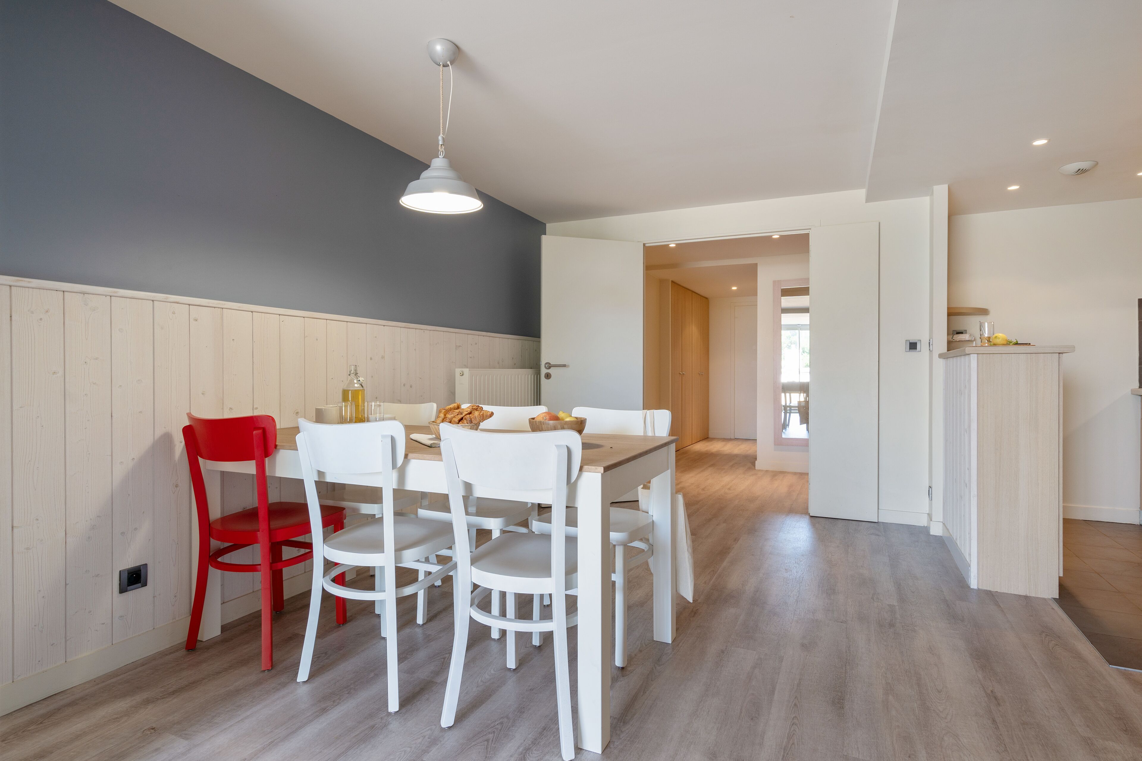 A modern kitchen with white cabinetry, a dining table with chairs, and a red chair.