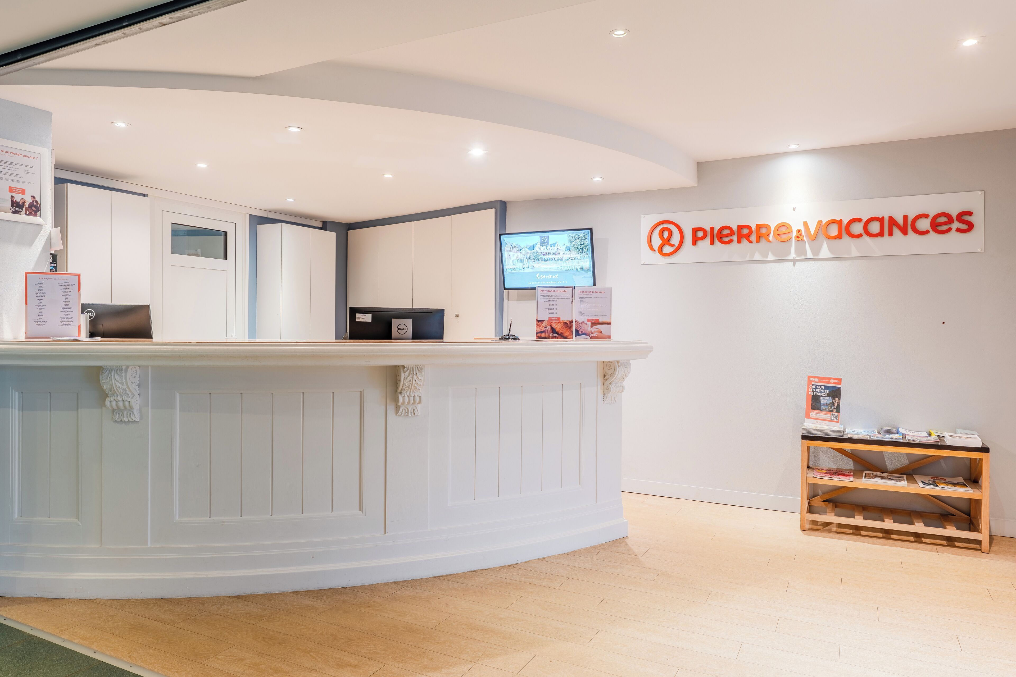 A reception desk with a flat-screen TV, a wooden shelf with brochures, and a sign reading "Pierre Vacances".