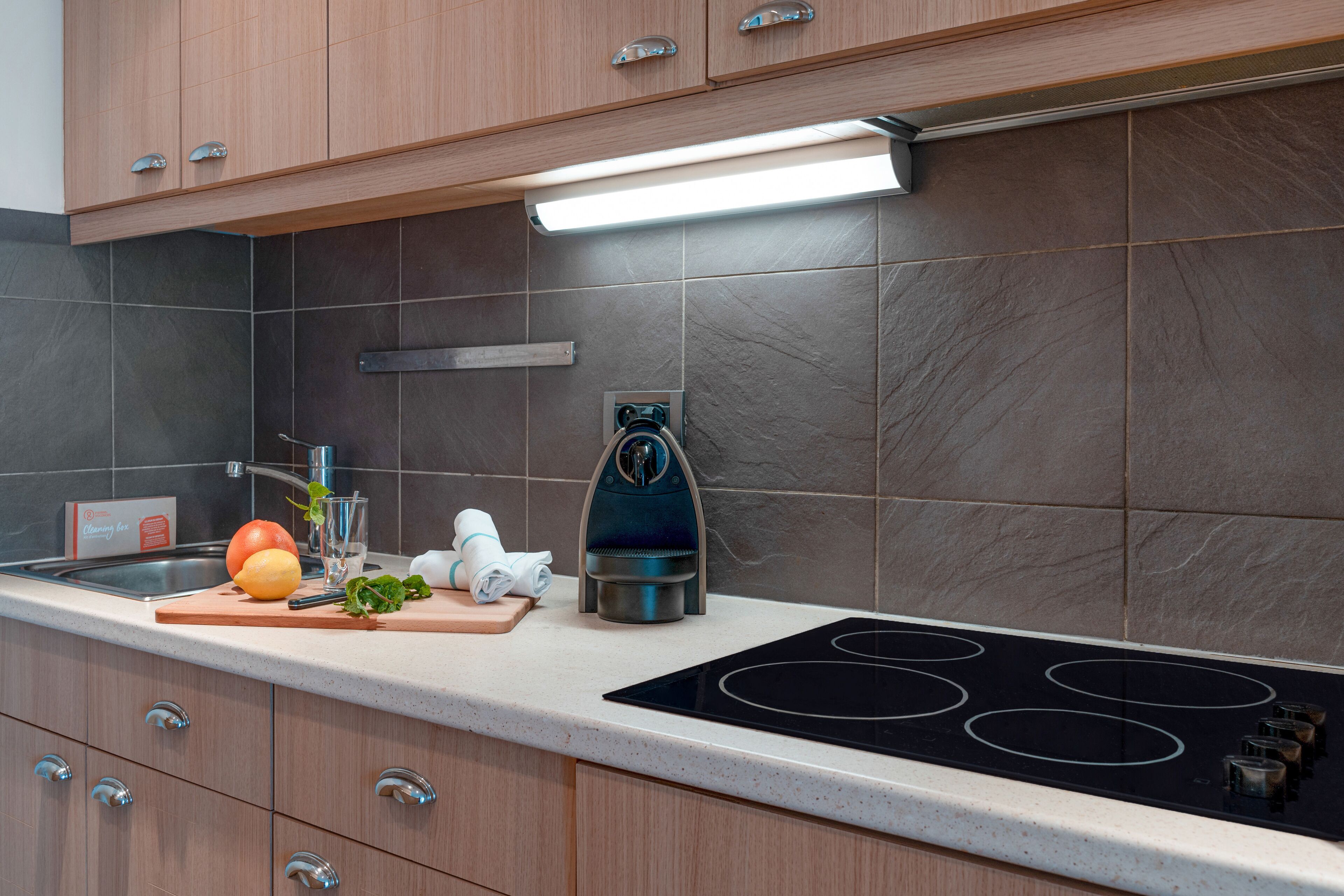 A modern kitchen with a stainless steel stove, wooden cabinets, and a countertop with a cutting board, vegetables, and a kettle.