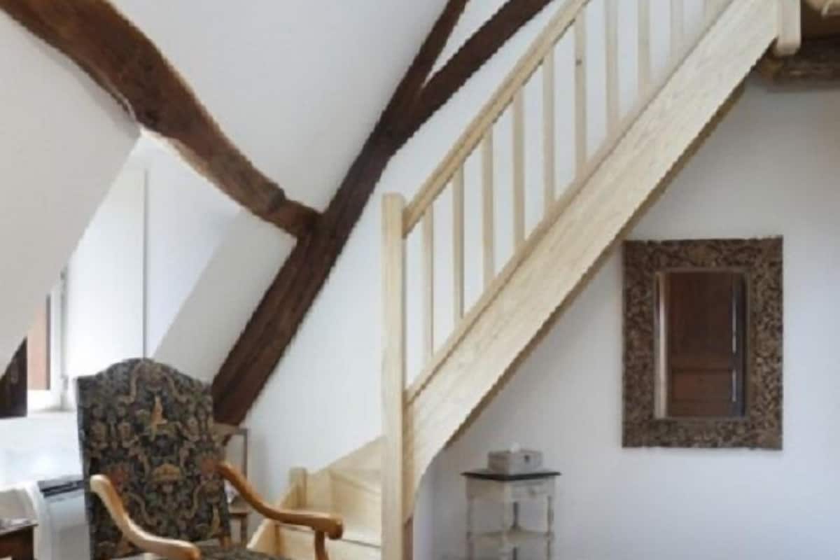 Een kamer met een houten stoel, een klein tafeltje en een trap met een houten leuning.