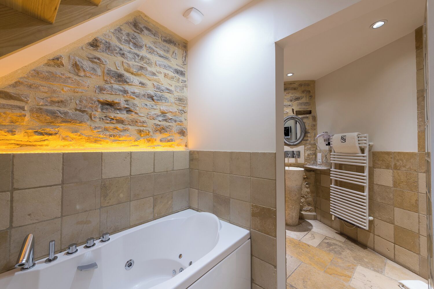 A modern bathroom with a stone wall, a bathtub, a shower area, and a towel rack.