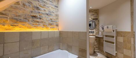 A modern bathroom with a stone wall, a bathtub, a shower area, and a towel rack.
