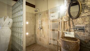 Un baño con cabina de ducha de vidrio, lavabo de madera, toallero y espejo en una pared de piedra.