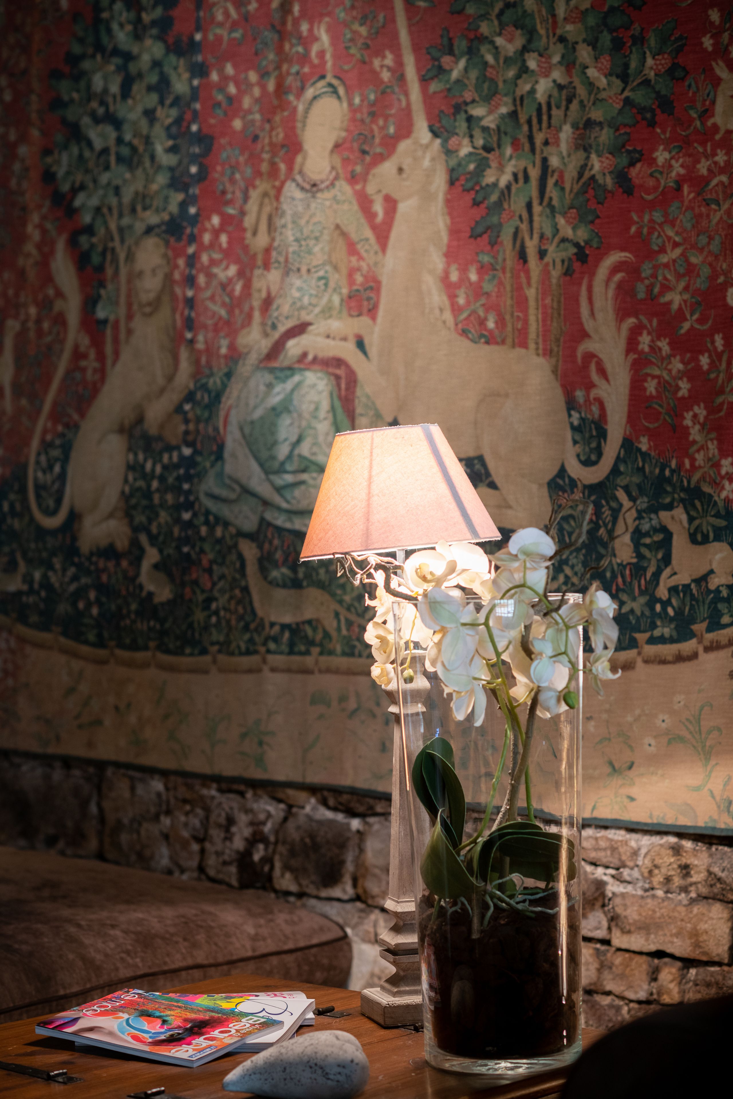A room with a tapestry, a lamp, and a potted plant.