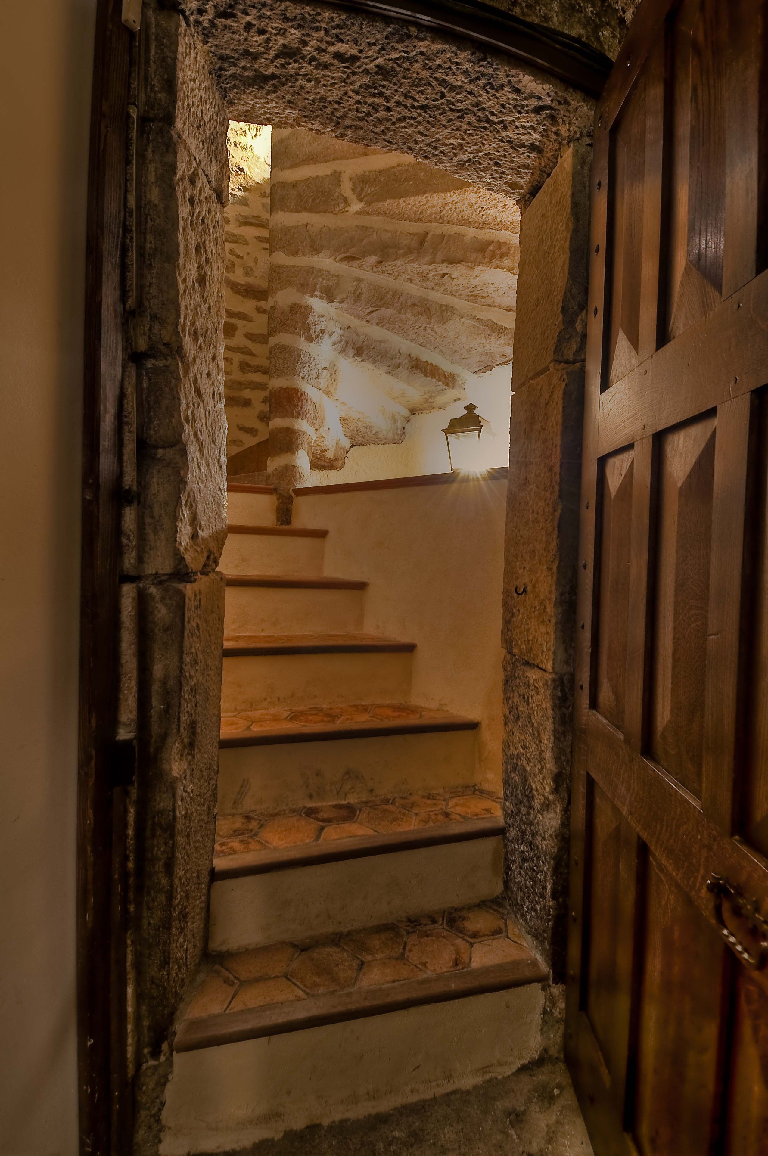 A stone staircase leading to a wooden door, with a textured ceiling and a small lantern above.