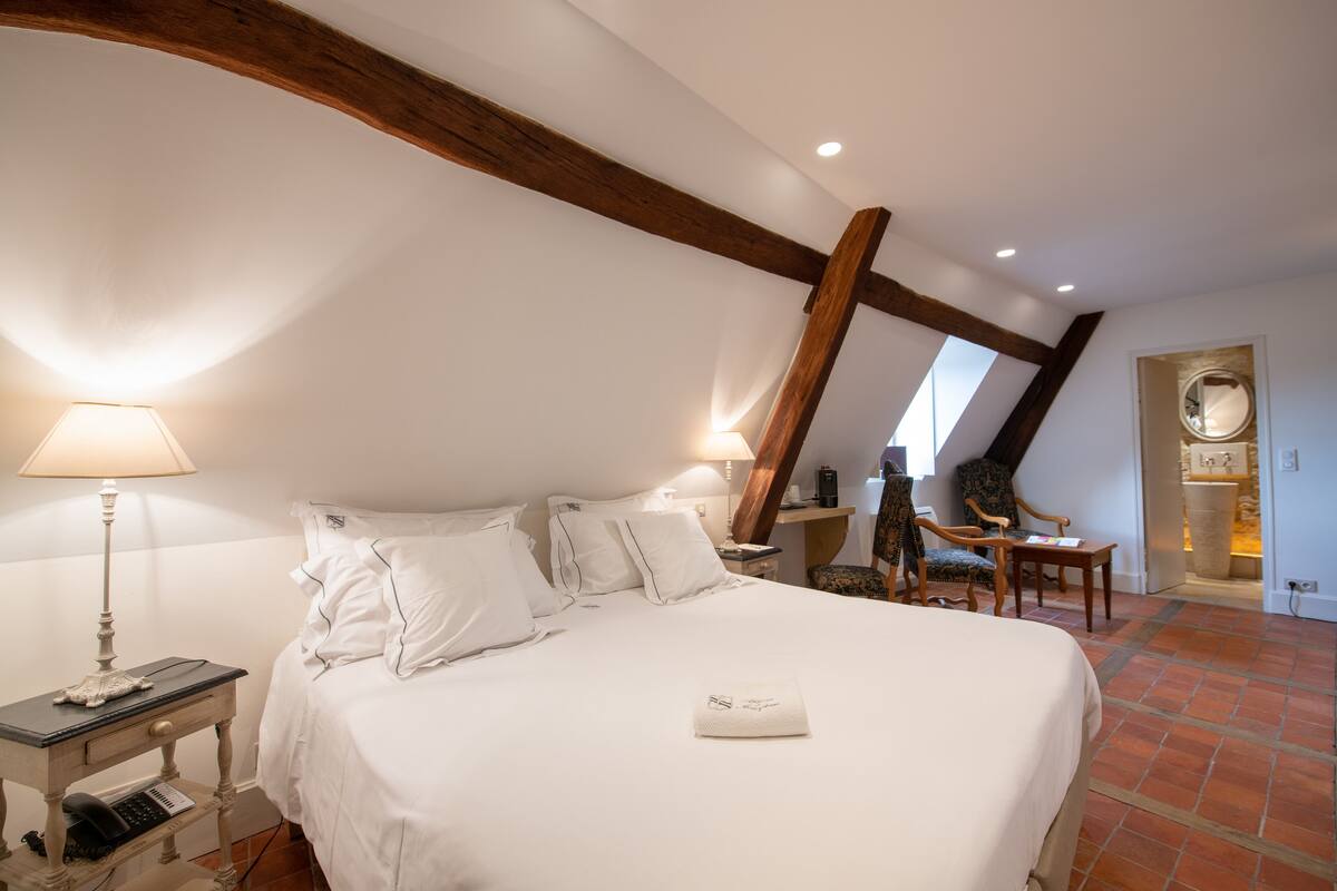 Een slaapkamer met een groot bed, nachtkastjes, een lamp en een stoel.